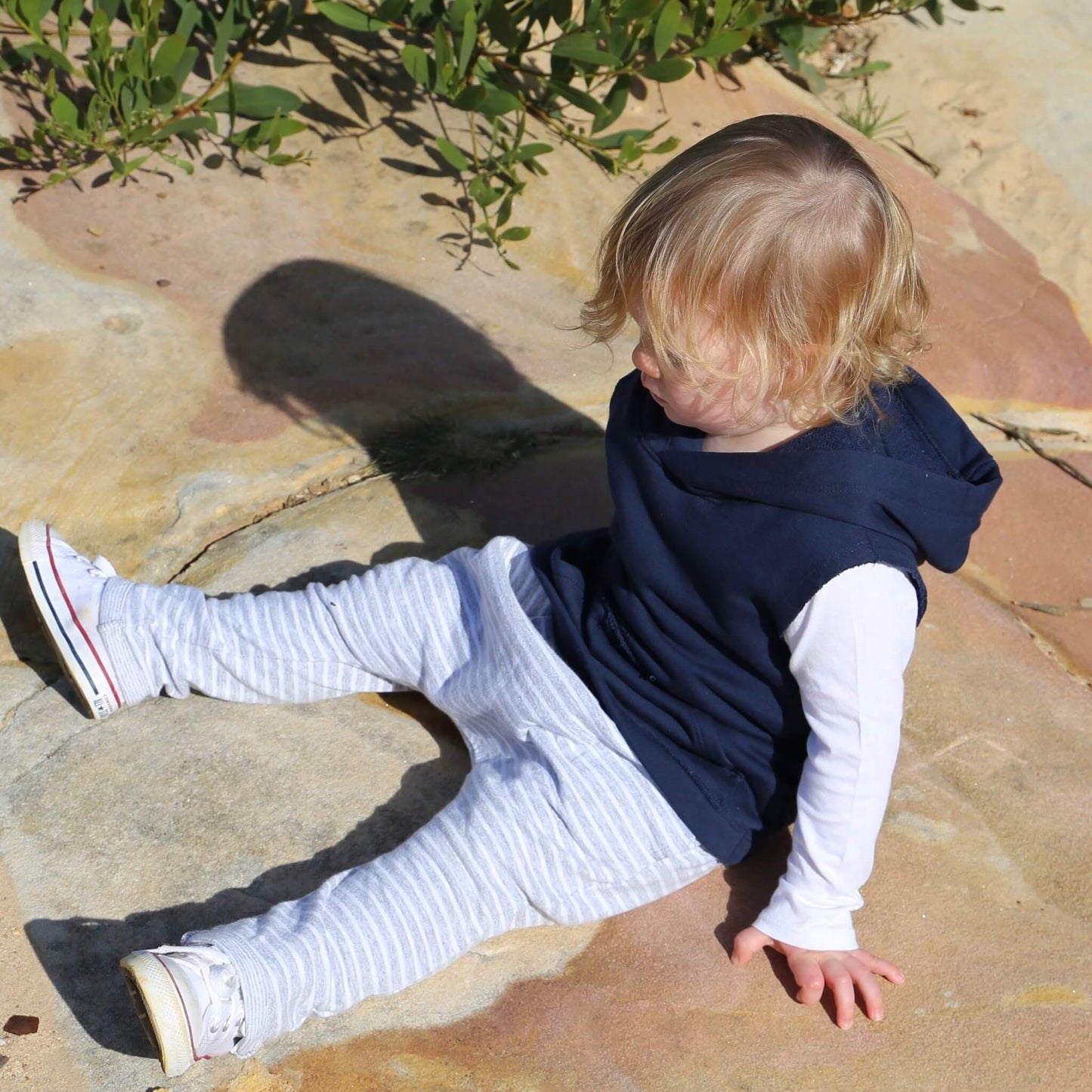 Toddler wearing Navy Sleeveless Hoodie ethically made in Australia with 100% Cotton French Terry featuring raw edge armhole and front pouch pocket with raw edges. Worn over White long sleeve tshirt with stripe Harem Pants
