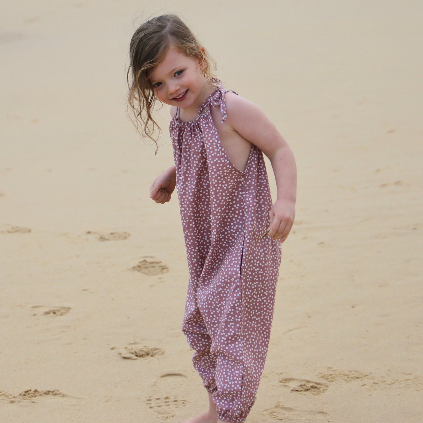 girl wearing antique rose/white spot romper featuring tie straps and elastic leg cuff. ethically made in australia with a linen cotton blend lightweight fabric