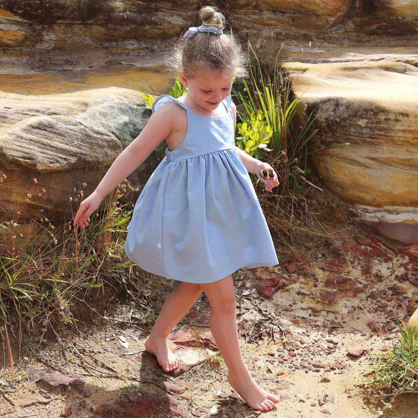 Girl wearing Sky Blue Dress featuring a gathered skirt and frill on back crossed straps. Ethically made in Australia with a Linen Cotton blend fabric