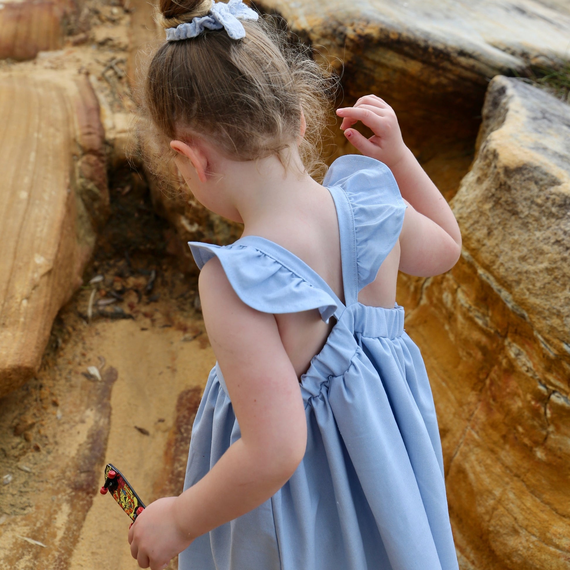 Girl wearing Sky Blue Dress featuring a gathered skirt and frill on back crossed straps. Ethically made in Australia with a Linen Cotton blend fabric