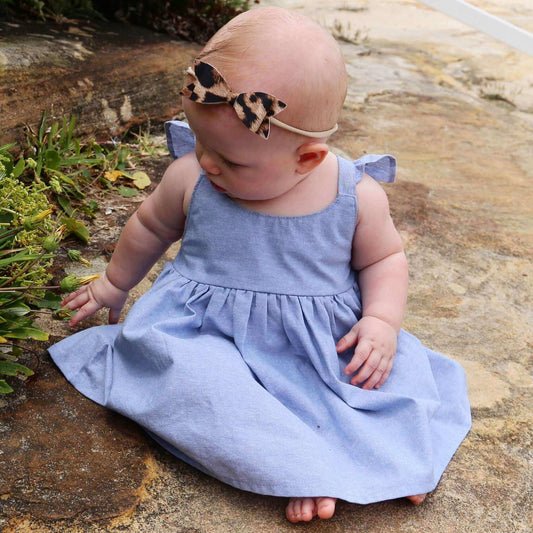 Baby Girl wearing Blue Dress featuring a gathered skirt and frill on back crossed straps. Ethically made in Australia with 100% Cotton Chambray fabric