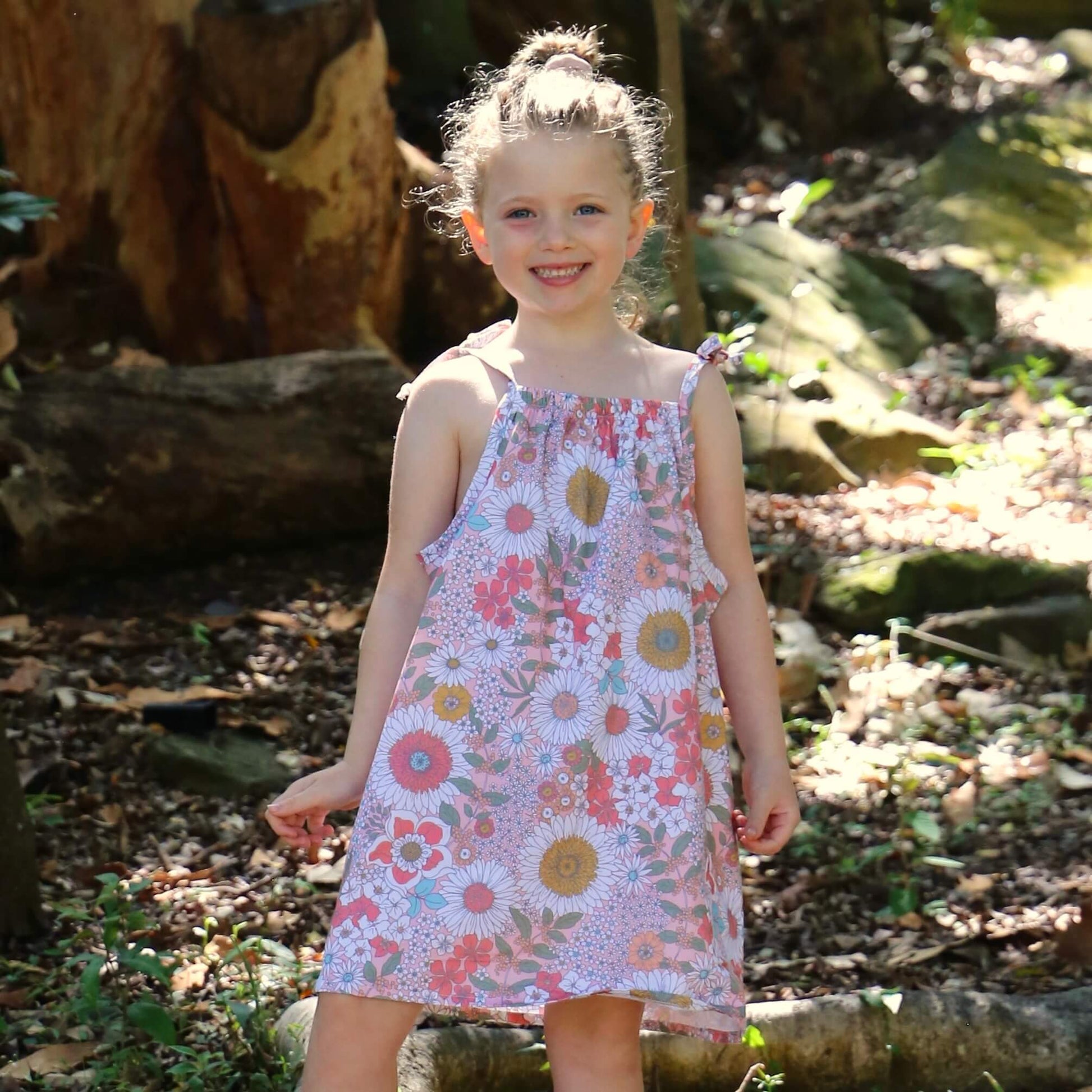 girl wearing Daisy printed cotton poplin a-line dress with shoulder strap ties.  Ethically made in australia with 100% printed cotton poplin