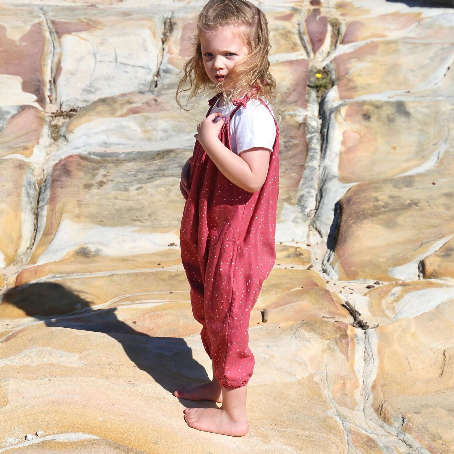 girl wearing rouge/white spot printed romper featuring tie straps and elastic leg cuff. ethically made in australia with 100% cotton drill.