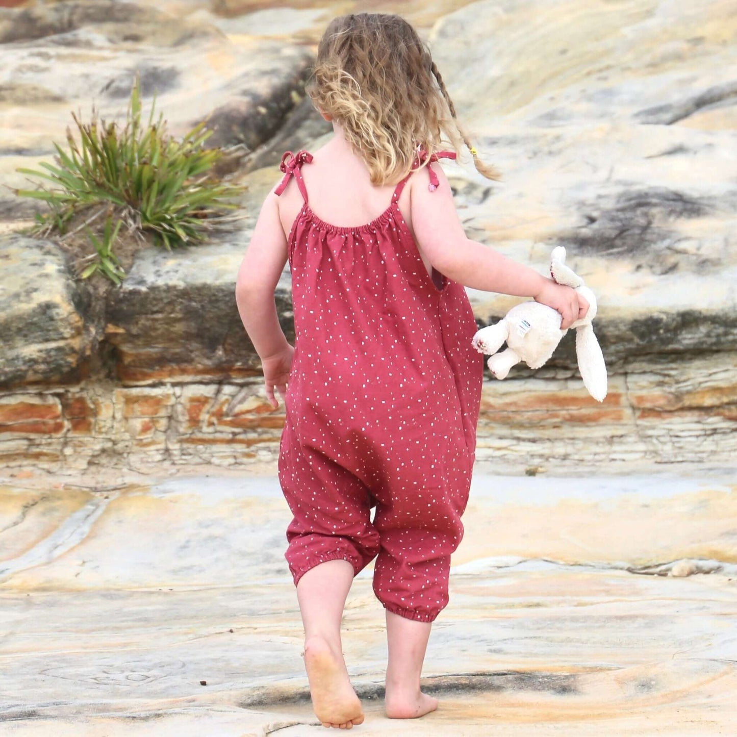 girl wearing rouge/white spot printed romper featuring tie straps and elastic leg cuff. ethically made in australia with 100% cotton drill.