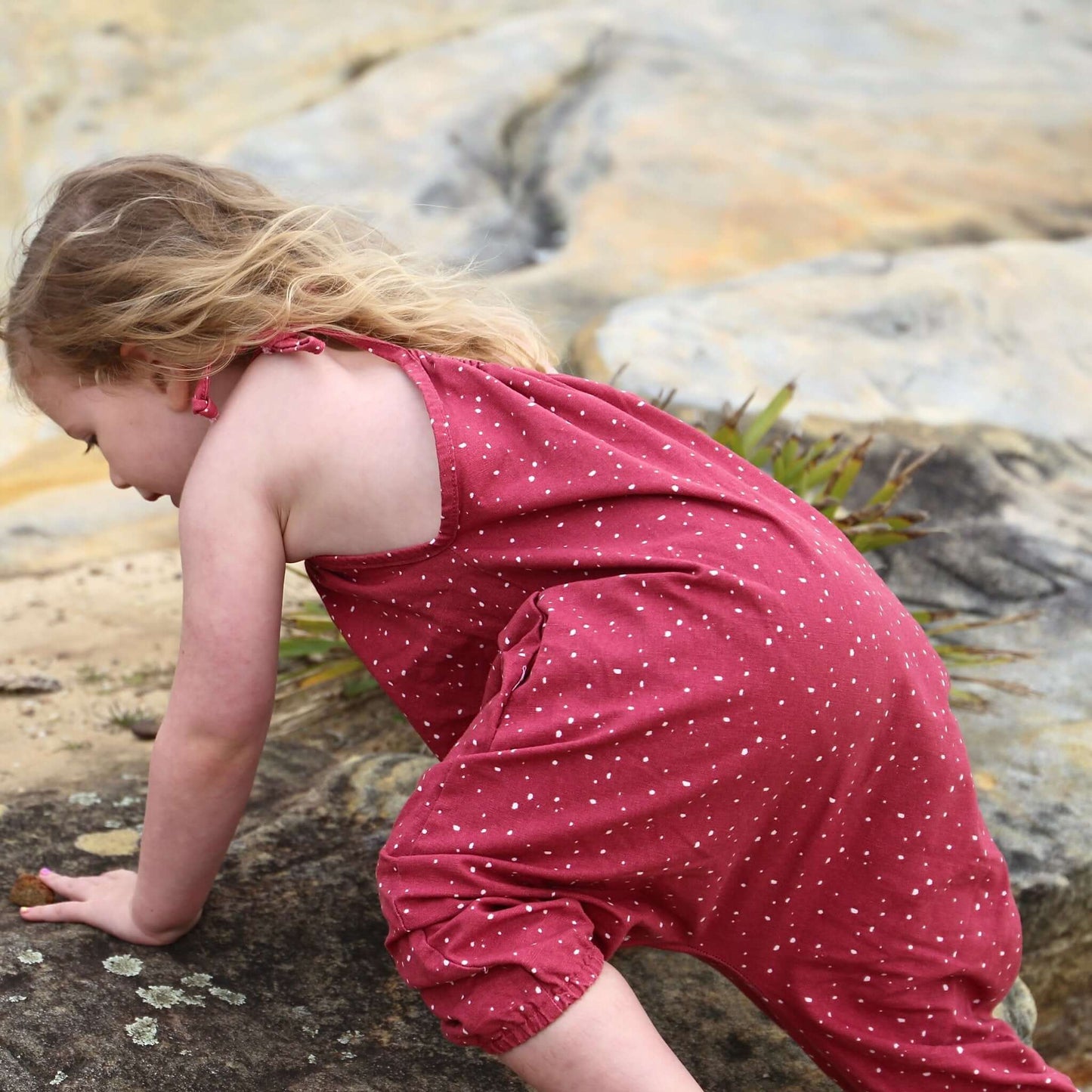 girl wearing rouge/white spot printed romper featuring tie straps and elastic leg cuff. ethically made in australia with 100% cotton drill.