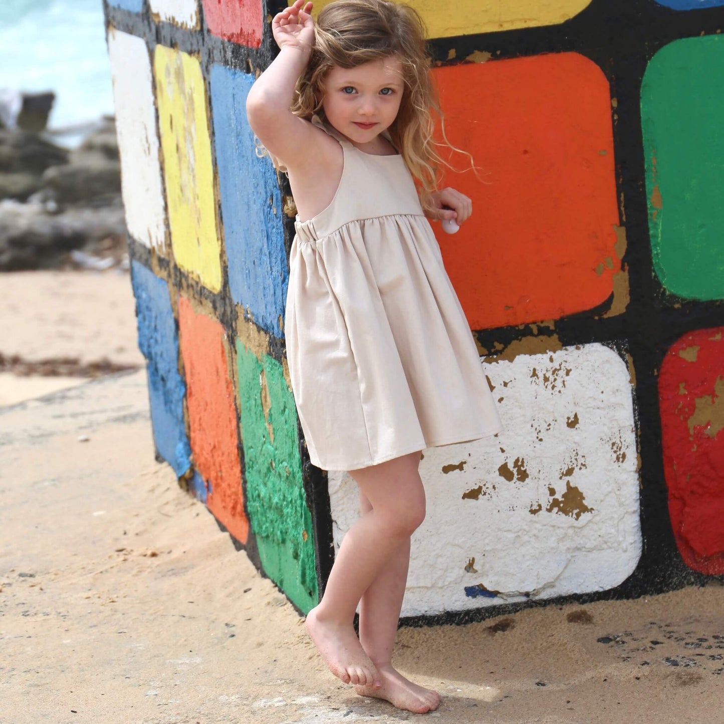 Girl wearing Linen colour Dress featuring a gathered skirt and frill on back crossed straps. Ethically made in Australia with a Linen Cotton blend fabric