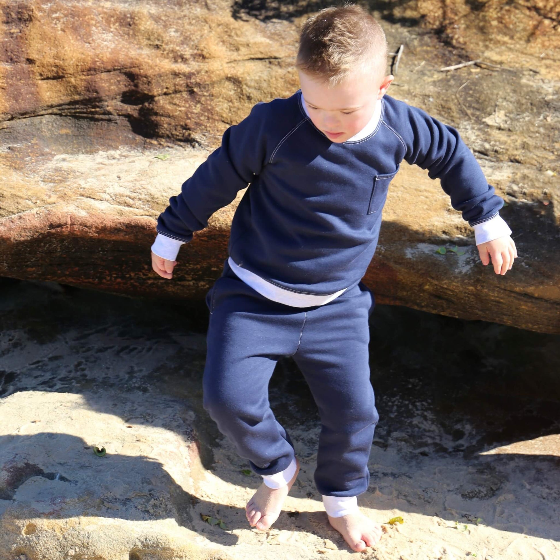 Boy wearing Navy Blue trackpant featuring White contrast waistband, hem cuffs and drawcord, side pockets. Ethically made in Australia with cotton blend cosy and warm fleece