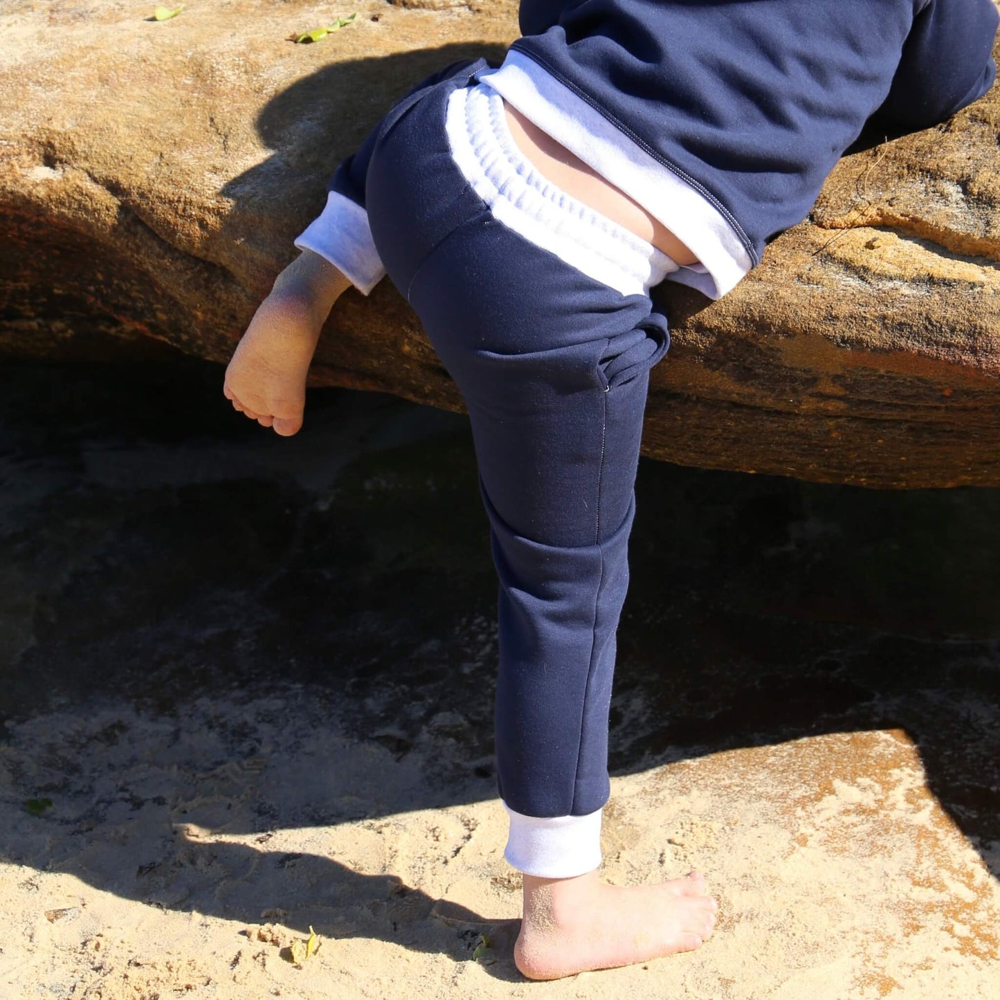 Boy wearing Navy Blue trackpant featuring White contrast waistband, hem cuffs and drawcord, side pockets. Ethically made in Australia with cotton blend cosy and warm fleece