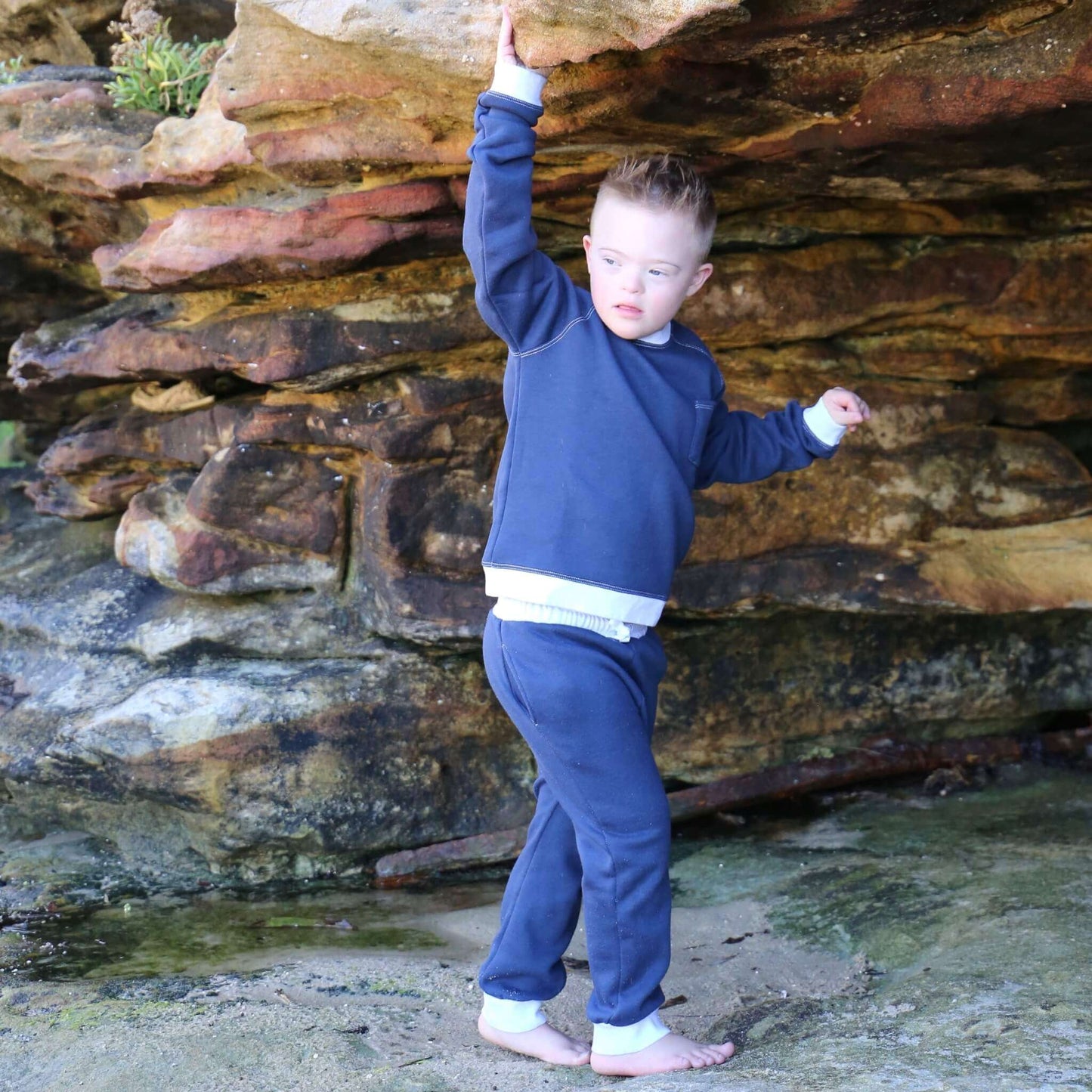 Boy wearing Navy Blue trackpant featuring White contrast waistband, hem cuffs and drawcord, side pockets. Ethically made in Australia with cotton blend cosy and warm fleece