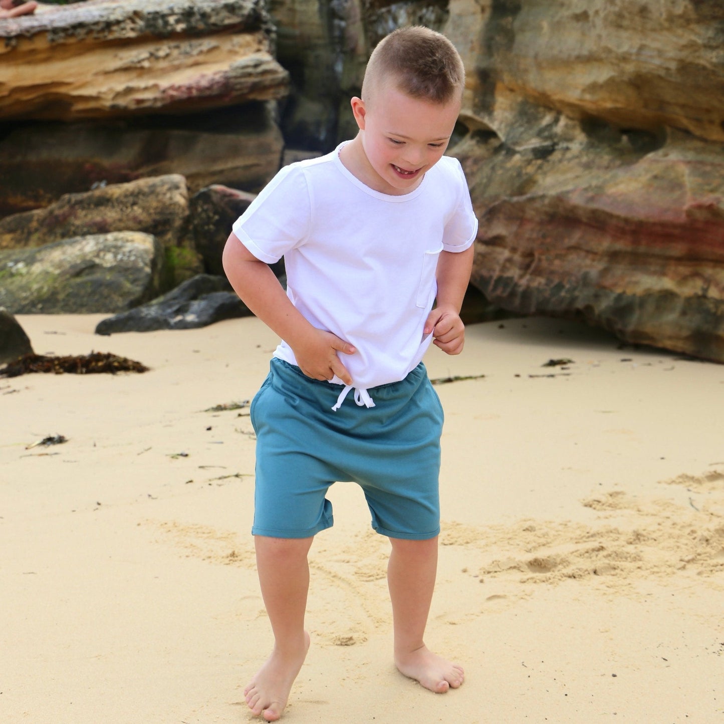 Boy wearing Ocean colour drop crotch shorts with contrast white drawcord and elastic waistband.  ethically made in australia with 100% cotton jersey.