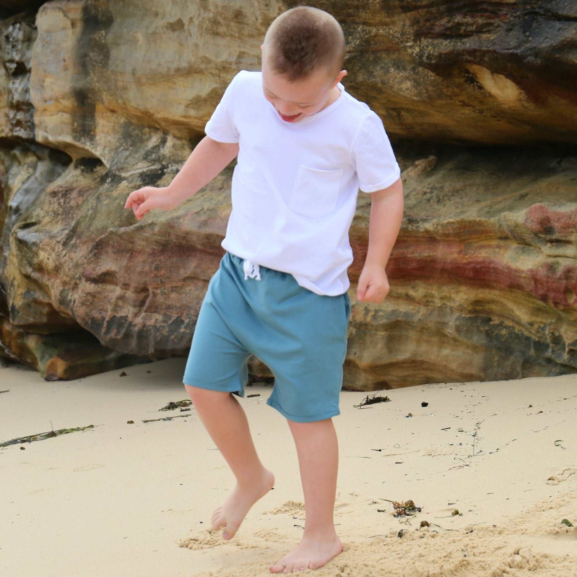 Boy wearing Ocean colour drop crotch shorts with contrast white drawcord and elastic waistband.  ethically made in australia with 100% cotton jersey.