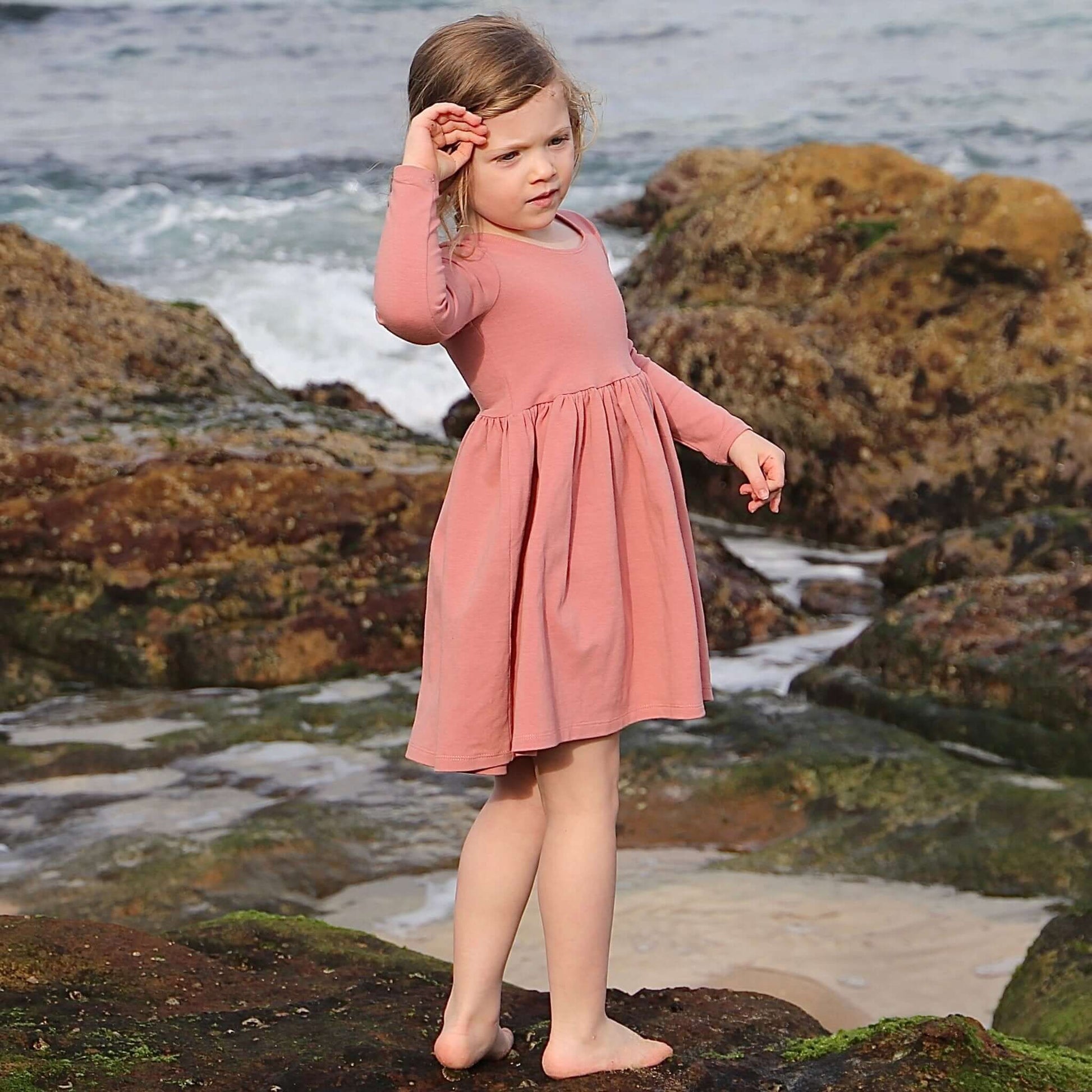 girl wearing rose colour long sleeve dress featuring low back and gathered waist skirt.  Ethically made in australia with a organic cotton jersey fabric.