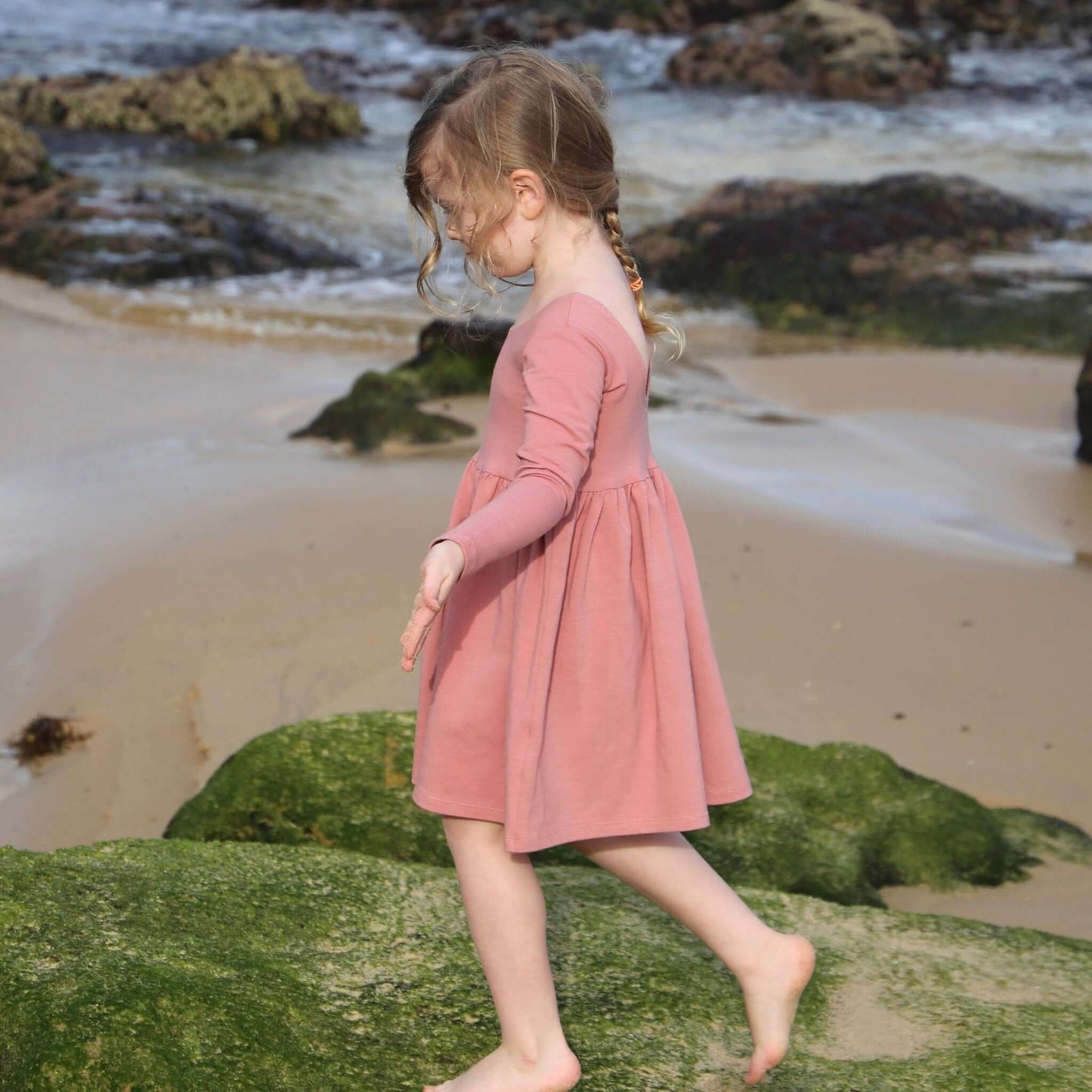 girl wearing rose colour long sleeve dress featuring low back and gathered waist skirt.  Ethically made in australia with a organic cotton jersey fabric.