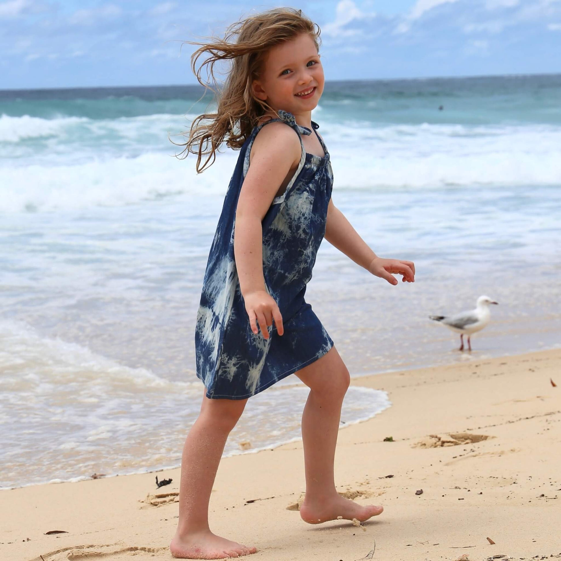 girl wearing tie dye a-line dress with shoulder strap ties.  Ethically made in australia with 100% printed cotton chambray