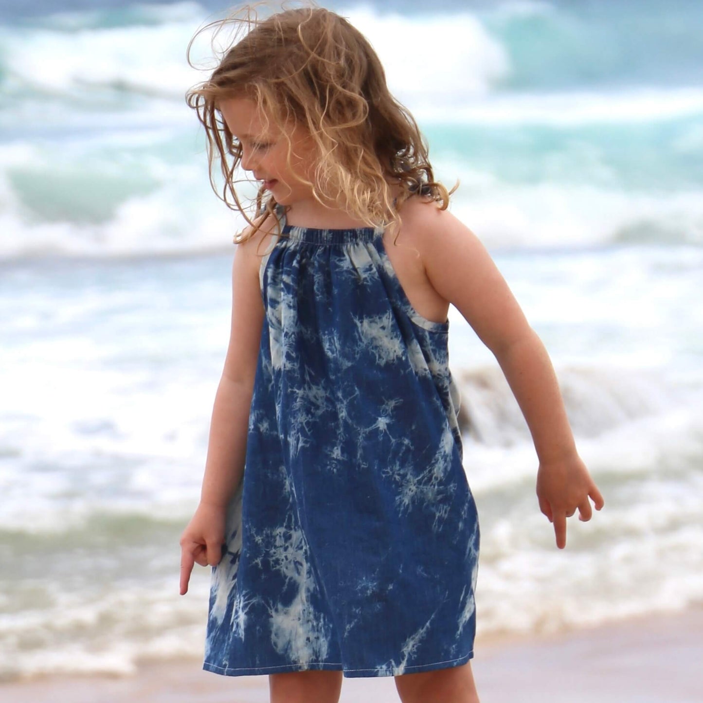 girl wearing tie dye a-line dress with shoulder strap ties.  Ethically made in australia with 100% printed cotton chambray