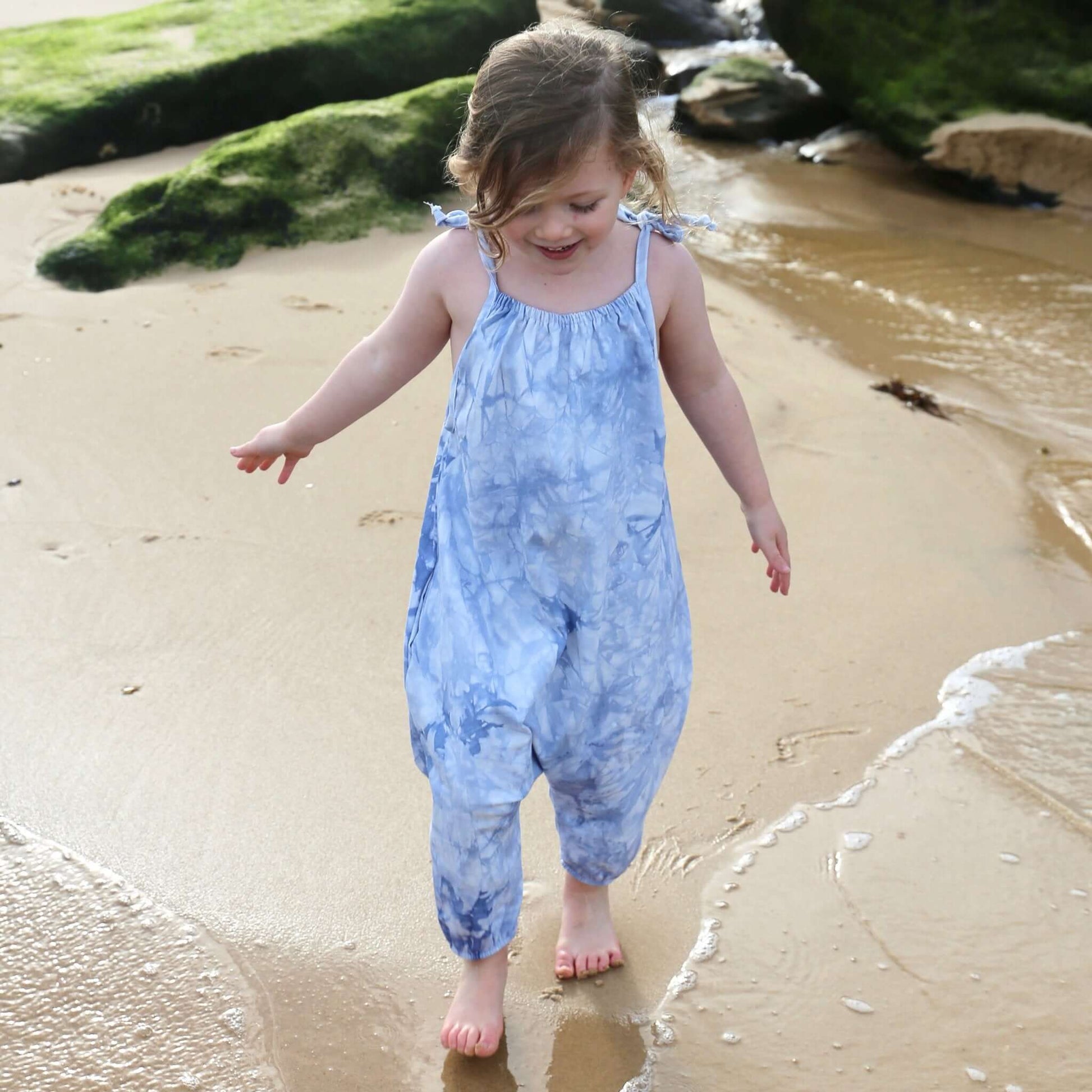 girl wearing light blue tie dye romper featuring tie straps and elastic leg cuff. ethically made in australia with stretch cotton drill