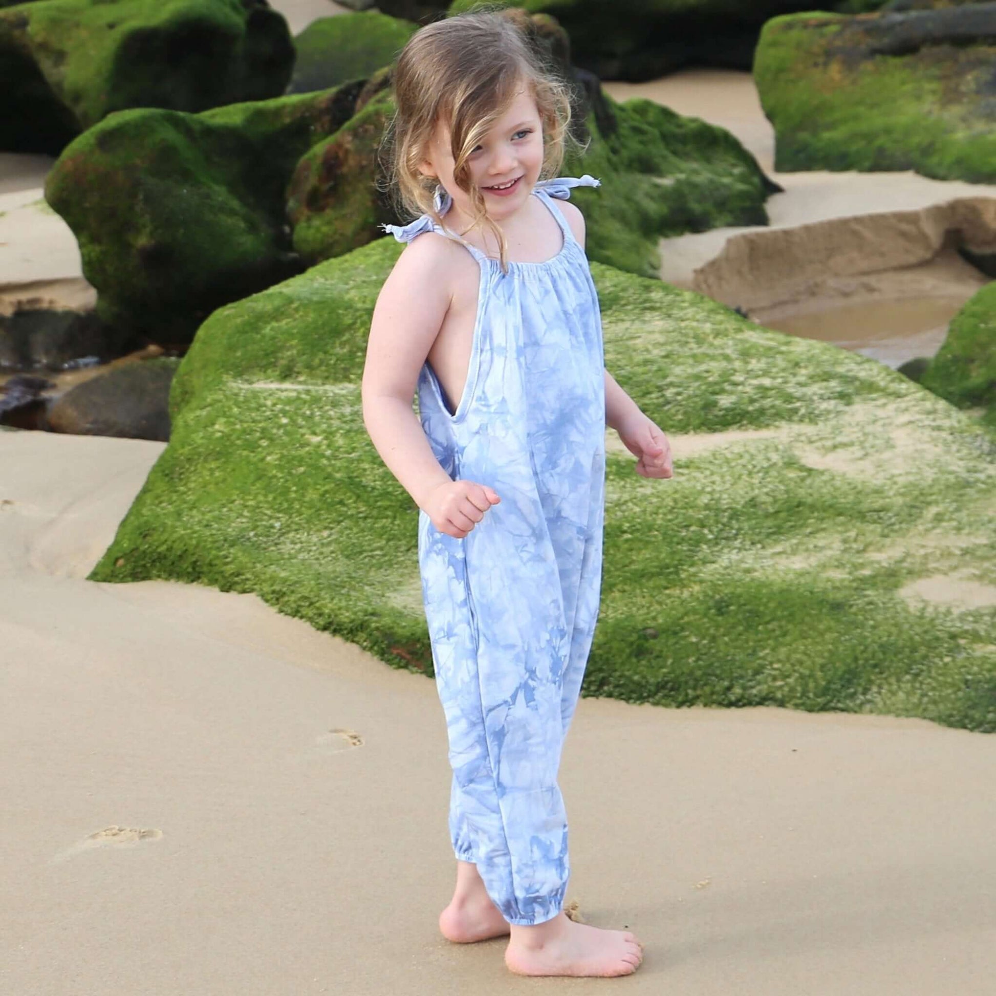 girl wearing light blue tie dye romper featuring tie straps and elastic leg cuff. ethically made in australia with stretch cotton drill