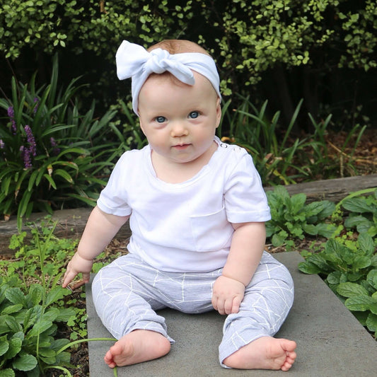 baby girl wearing white short sleeve tshirt featuring front pocket, turned up cuffs and raw edge neckline. Ethically made in australia with 100% cotton jersey