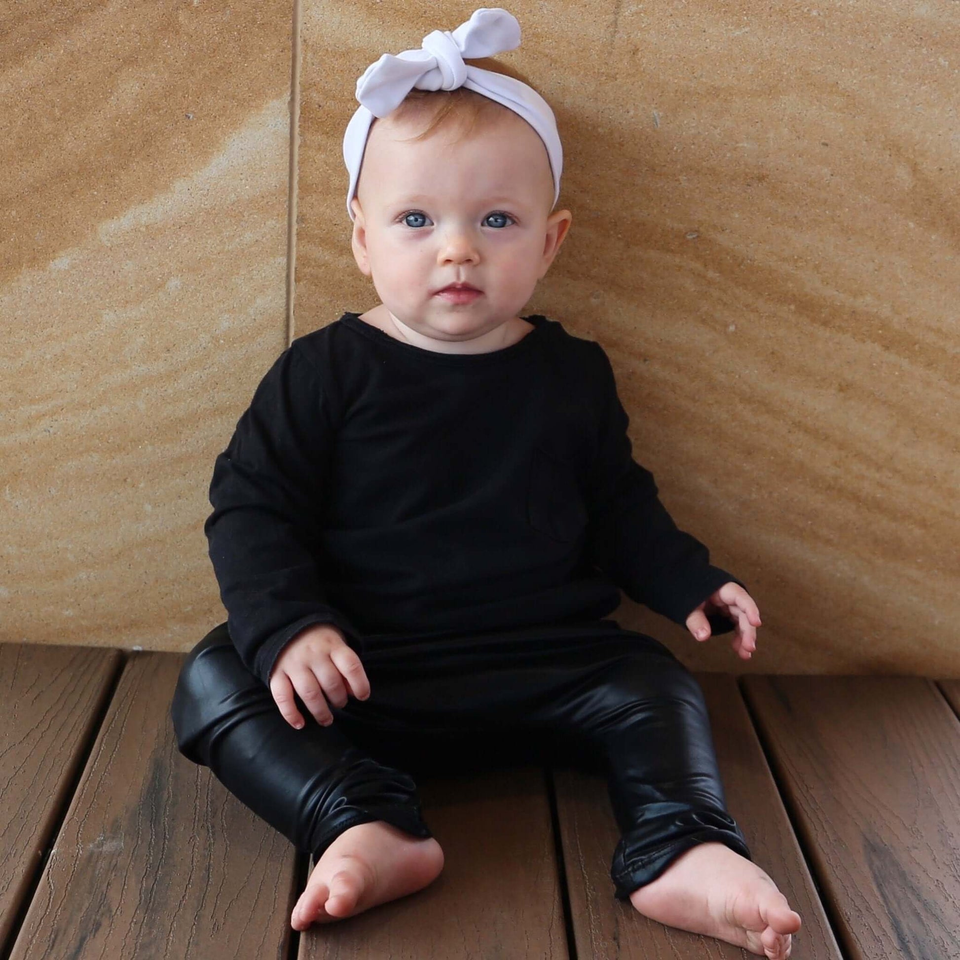 baby girl wearing black long sleeve tshirt featuring front pocket and raw edge neckline. Ethically made in australia with 100% cotton jersey