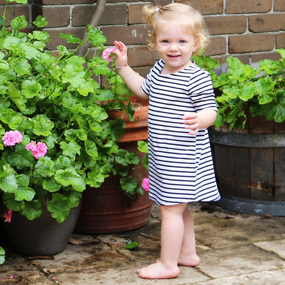 toddler girl wearing white with black stripe casual dress featuring 3/4 sleeves. Ethically made in australia with a cotton/elastane jersey fabric. Dress length sits at knee.