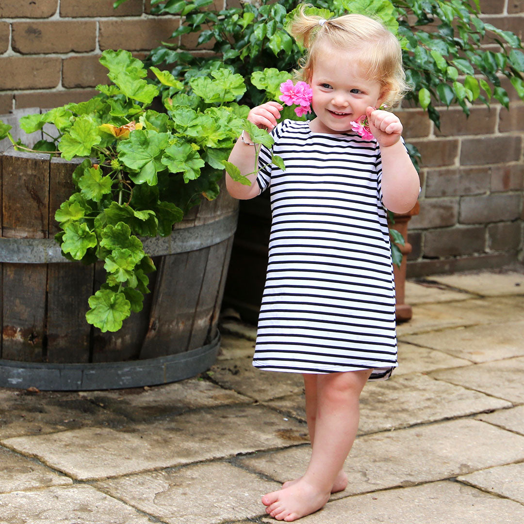 toddler girl wearing white with black stripe casual dress featuring 3/4 sleeves. Ethically made in australia with a cotton/elastane jersey fabric. Dress length sits at knee.