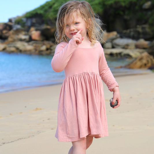 girl wearing peach colour long sleeve dress featuring low back and gathered waist skirt.  Ethically made in australia with a stretch cotton jersey fabric.