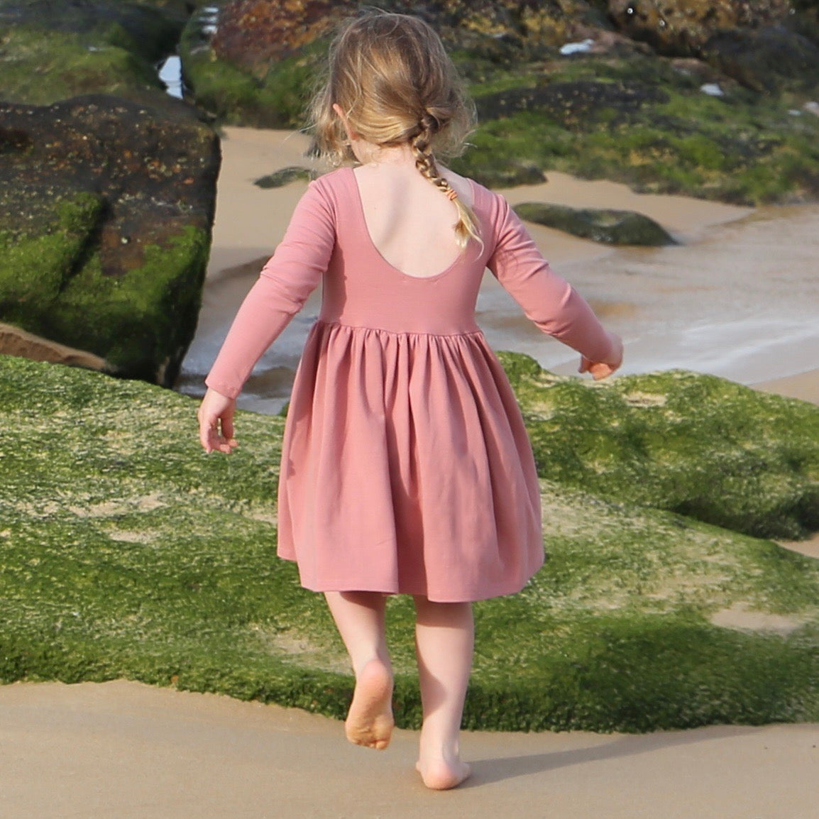 girl wearing rose colour long sleeve dress featuring low back and gathered waist skirt.  Ethically made in australia with a organic cotton jersey fabric.